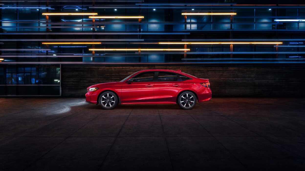Side wide view of a parked red Civic Sedan in a dark warehouse-like space.