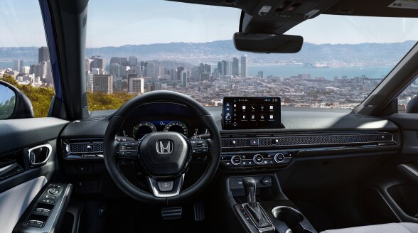 Panoramic view through the windshield, overlooking a waterfront cityscape. 