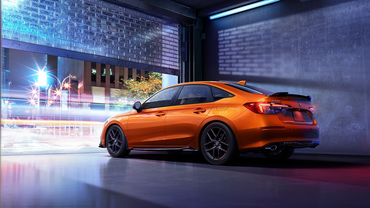 3/4 rear sideview of orange Civic Si about to leave a condo underground parking garage into a city street at night.