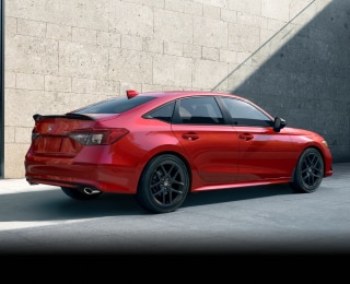 Rear sideview of a red Civic Si parked in front of a stone-walled building.