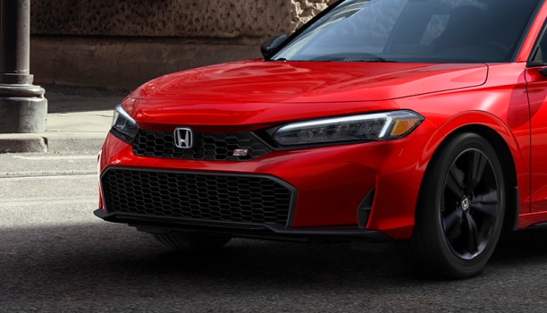 Gros plan du phare d’une Civic Si rouge circulant en ville.