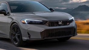 3/4 front closeup view of grey Civic Si driving on straight mountainous highway. 