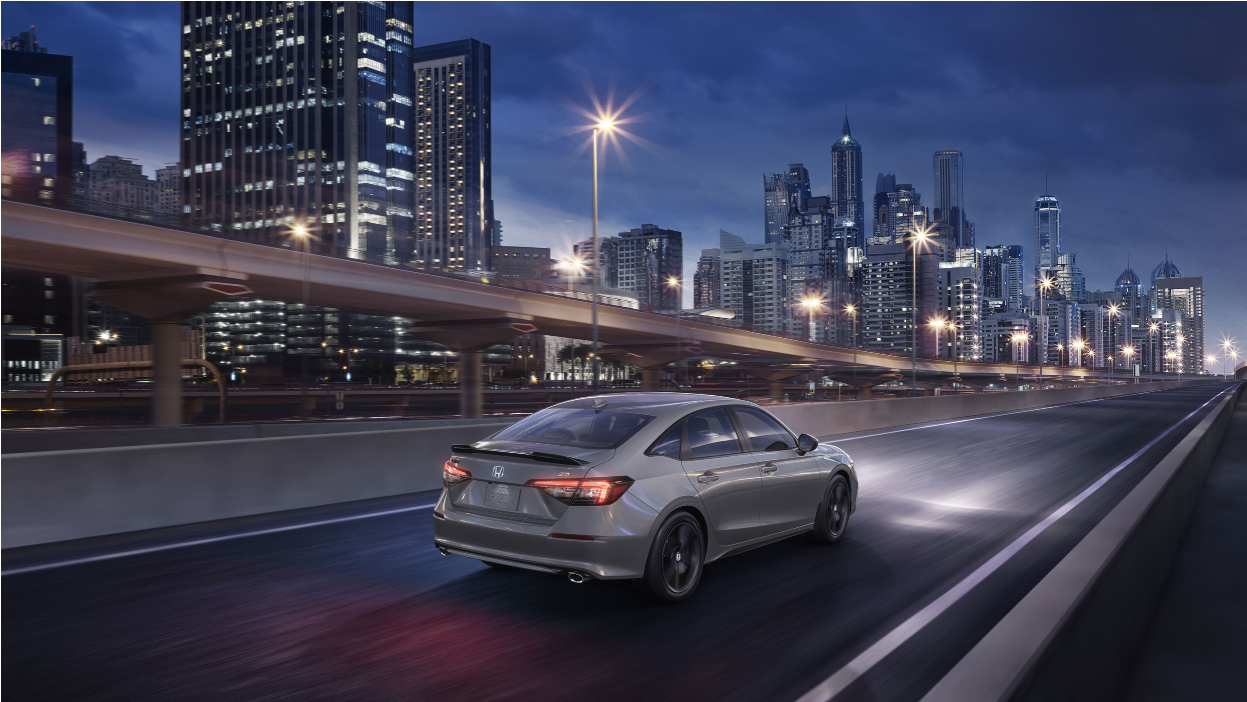 Vue 3/4 latérale en plongée d’une Civic Si grise sur une autoroute surplombant une ville.