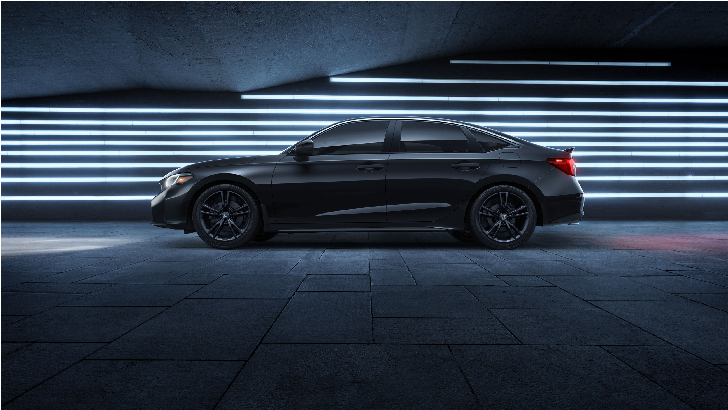 Vue latérale d’une Civic Si noire stationnée devant des lumières au néon bleues.