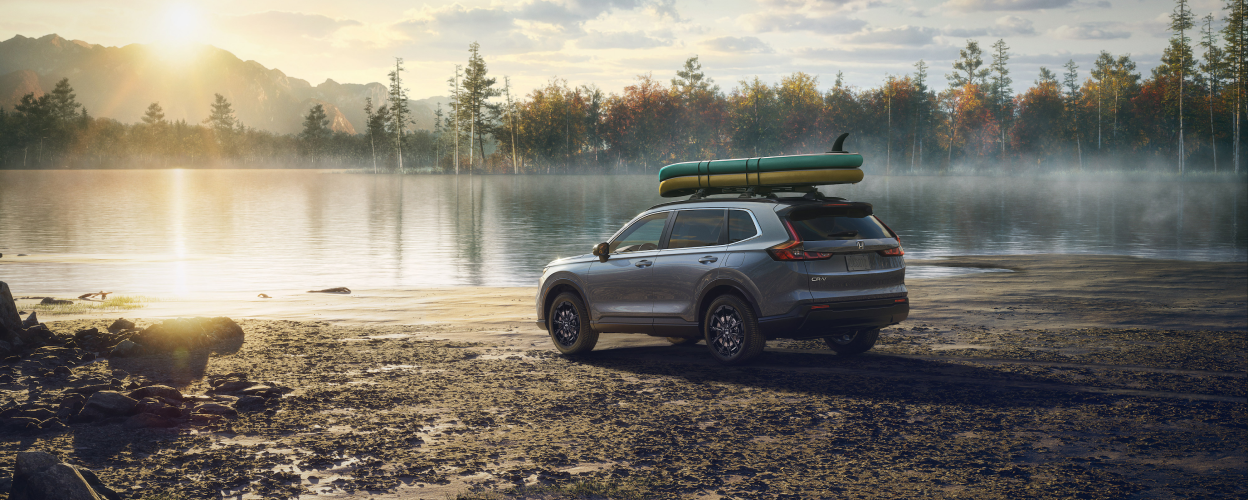 3/4 rear sideview of grey CR-V, with two paddle boards on the roof racks, parked on a lake shoreline on a dewy morning.
