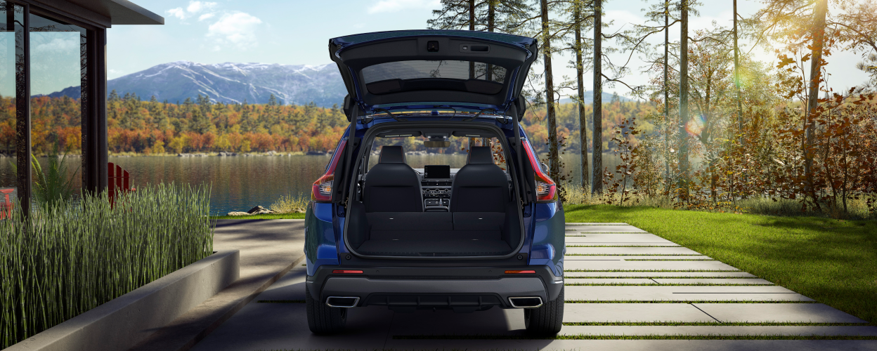 Rear view of open tailgate on a parked blue 2023 CR-V; lake and fall-coloured trees as backdrop.