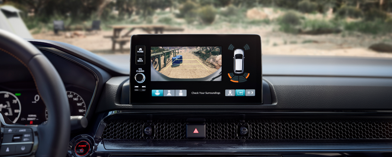 Closeup of touchscreen display showing what the rearview camera sees: two coolers behind the car on a dirt desert road. 