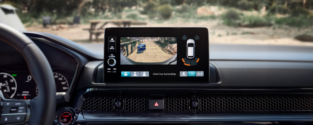 Closeup of touchscreen display showing what the rearview camera sees: two coolers behind the car on a dirt desert road.