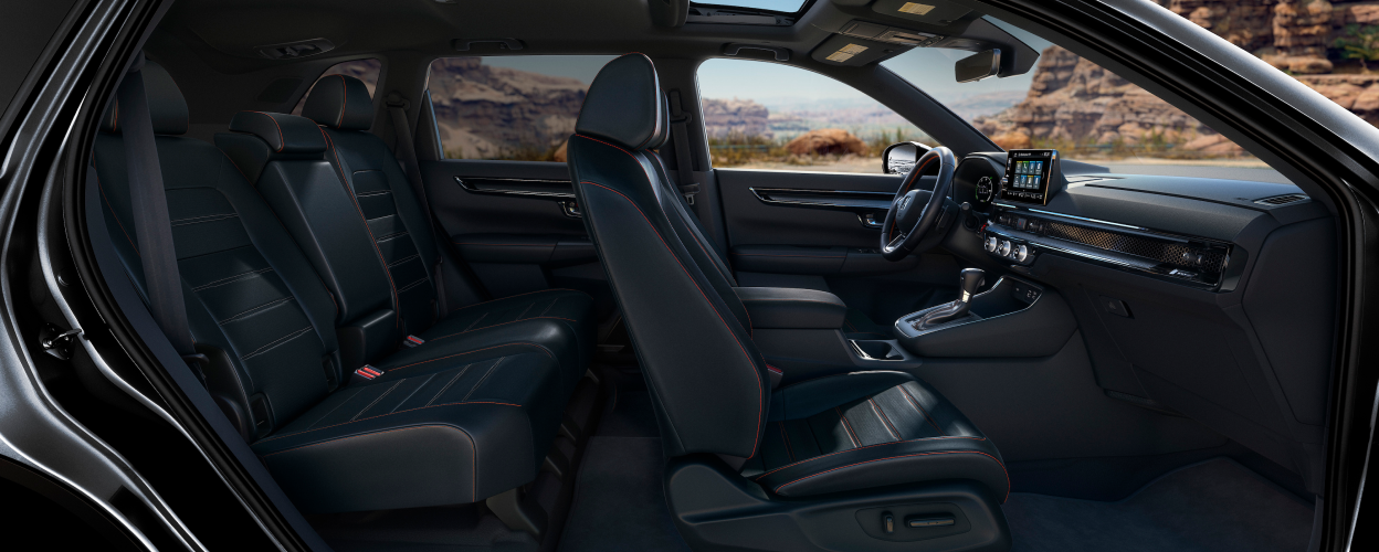 Panoramic sideview of the front and rear black seats with orange stitching in a grey CR-V parked in the desert.