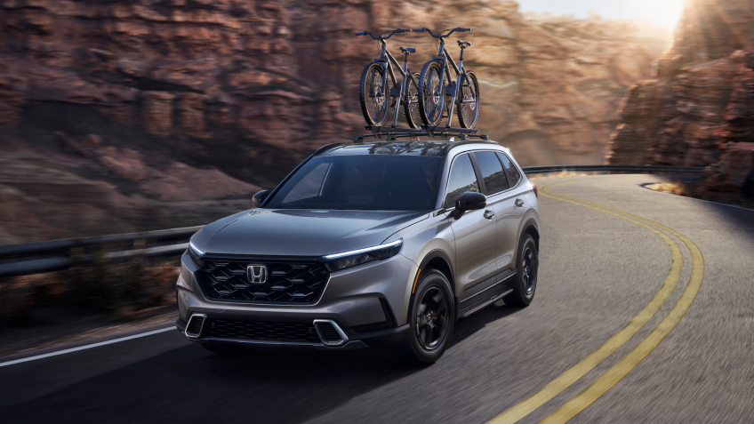 3/4 front view of grey CR-V, with two bikes on the roof racks, driving on a winding desert canyon highway. 