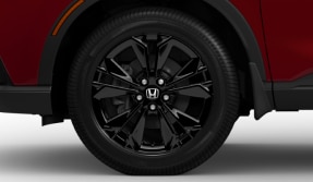  Sideview of the front of a red CR-V, highlighting its black aluminum-alloy wheel. 