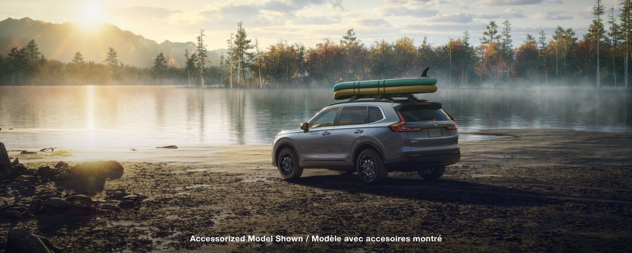 3/4 rear sideview of grey CR-V, with two paddle boards on the roof racks, parked on a lake shoreline on a dewy morning.