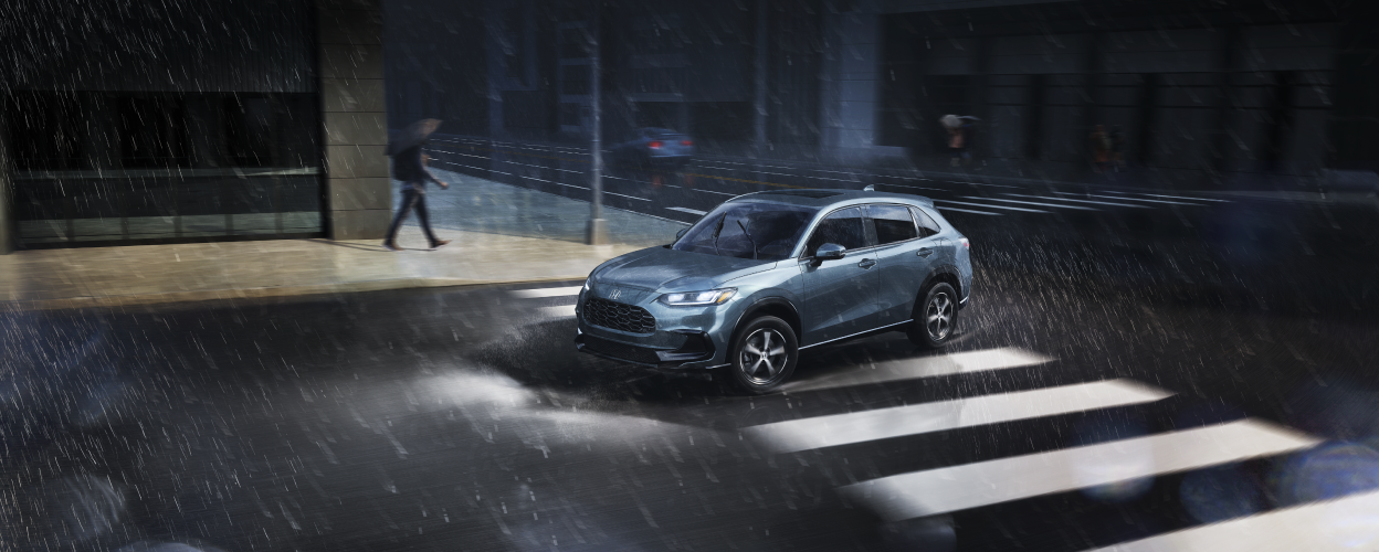 3/4 sideview of blueish grey HR-V driving in the rain in the city.