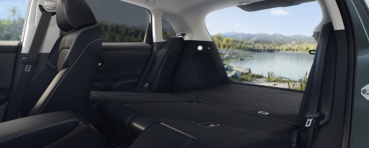 Wide view of a folded-down back seat and open tailgate, showcasing the cargo space in an HR-V. Lake in the background.  