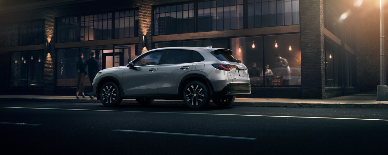 Vue latérale d’un HR-V gris stationné à l’extérieur d’un restaurant tendance en brique le soir.