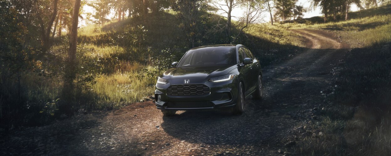 Vue 3/4 avant d’un HR-V noir roulant vers la caméra sur une route de terre en campagne.