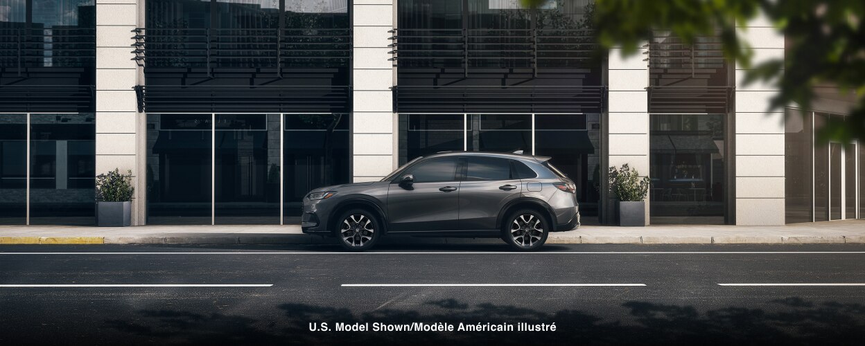 Vue latérale d’un HR-V gris stationné à l’extérieur d’un bâtiment contemporain en ville.