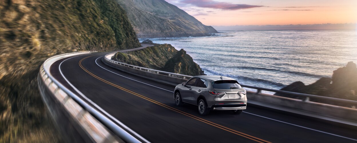 Vue 3/4 arrière d’un HR-V gris roulant sur une route côtière.