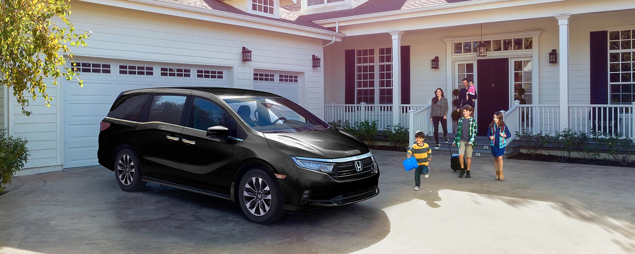 3/4 front side view of black Honda Odyssey parked in driveway. Family walking toward it.
