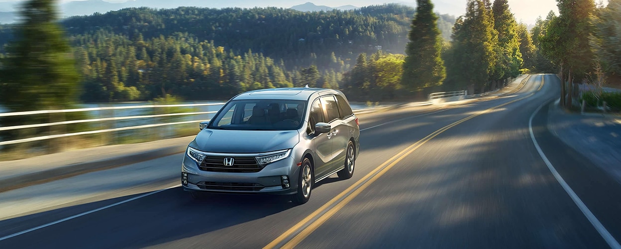 3/4 front view of grey Honda Odyssey driving on lakeside road.
