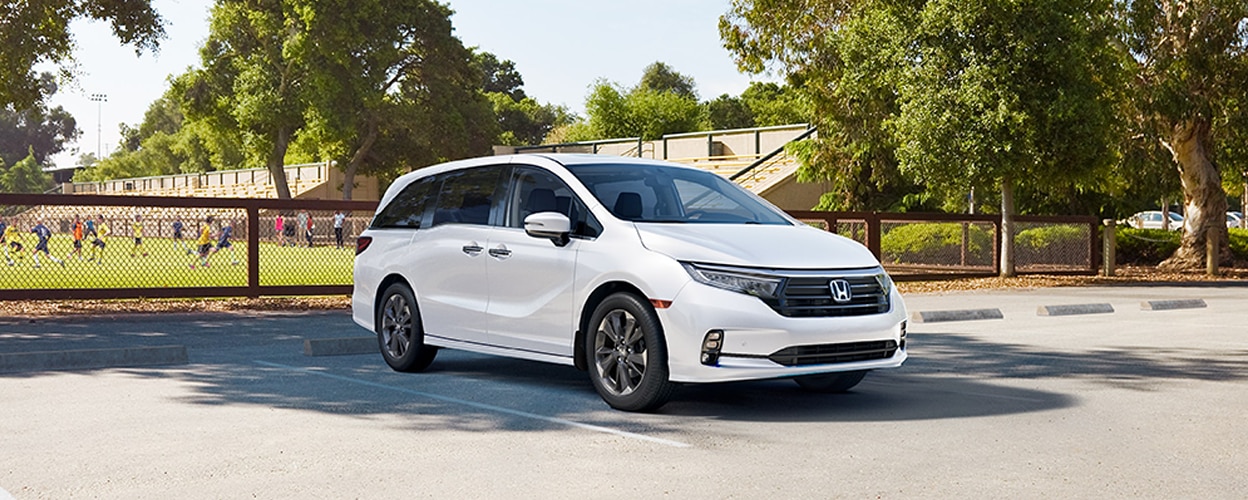 3/4 front view of white Honda Odyssey parked near a soccer field.
