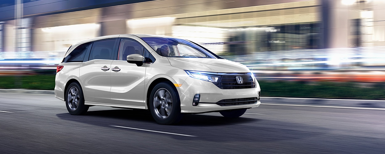 "3/4 side front view of white Honda Odyssey driving on city street at night. "