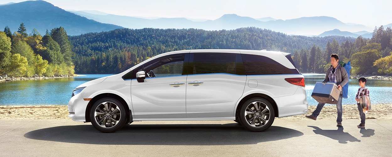 Sideview of white Honda Odyssey, parked lakeside. Dad and kid loading up the trunk. 