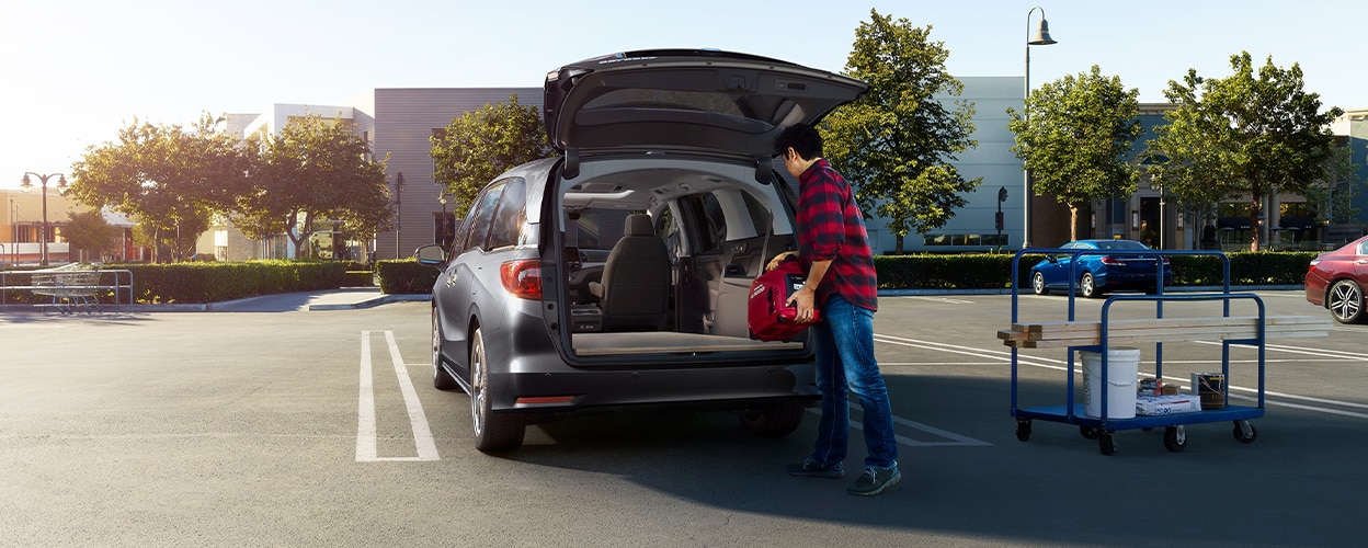 Man loading up Honda Odyssey trunk in empty parking lot.