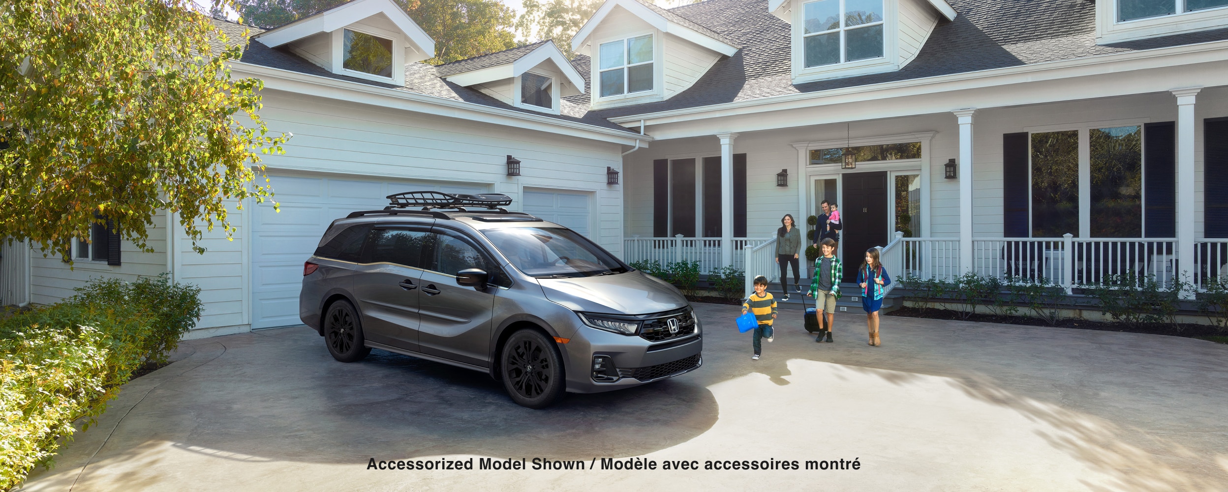 Vue latérale 3/4 avant d’une Odyssey grise stationnée dans une entrée. Une famille se dirige vers le véhicule.