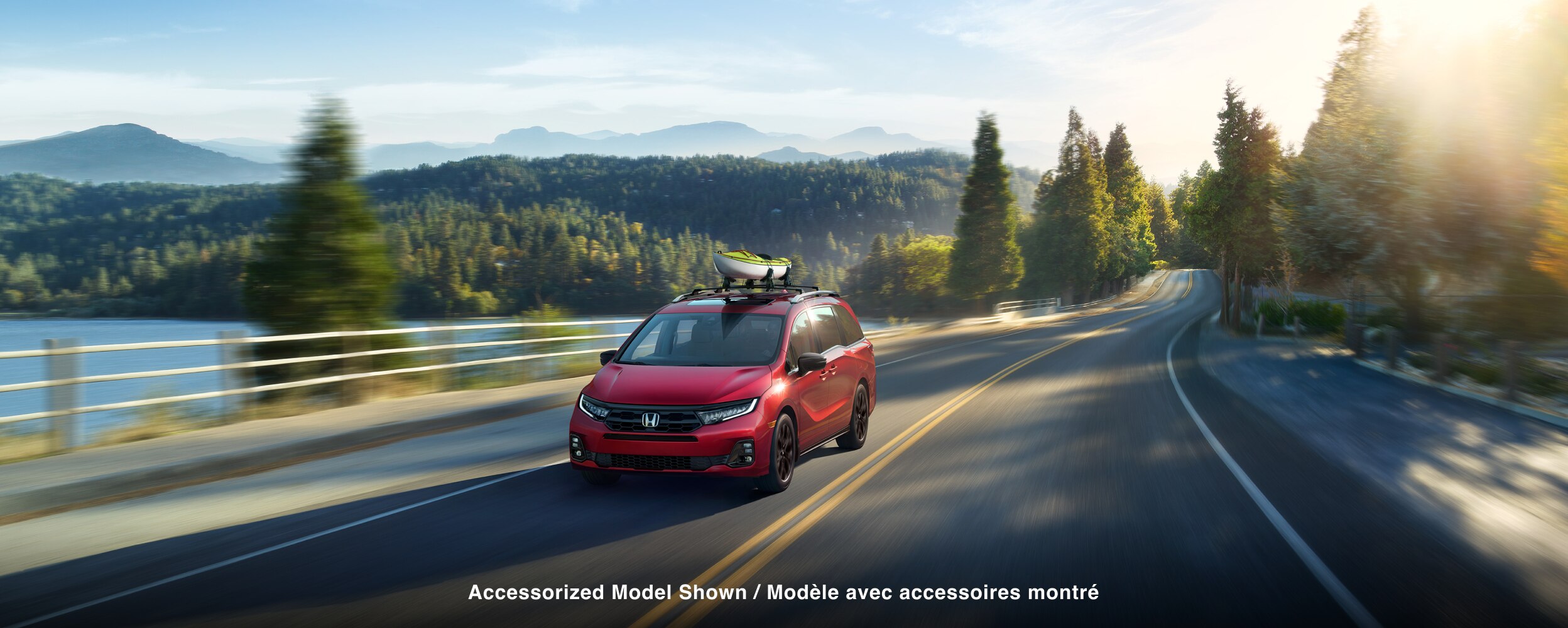 Vue 3/4 avant d’une Odyssey rouge sur une route au bord d’un lac.