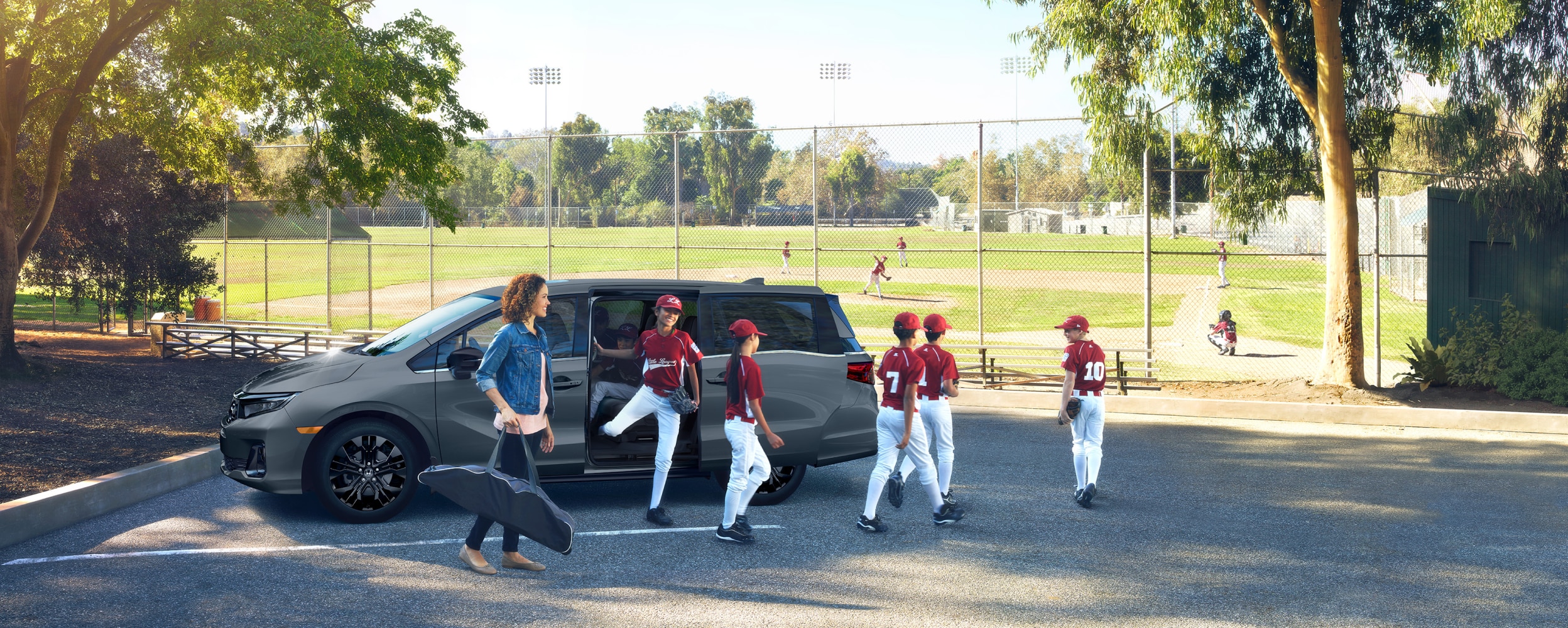 Une mère, ses enfants et leur équipe de baseball sortent d’une Odyssey grise stationnée près d’un terrain de baseball.