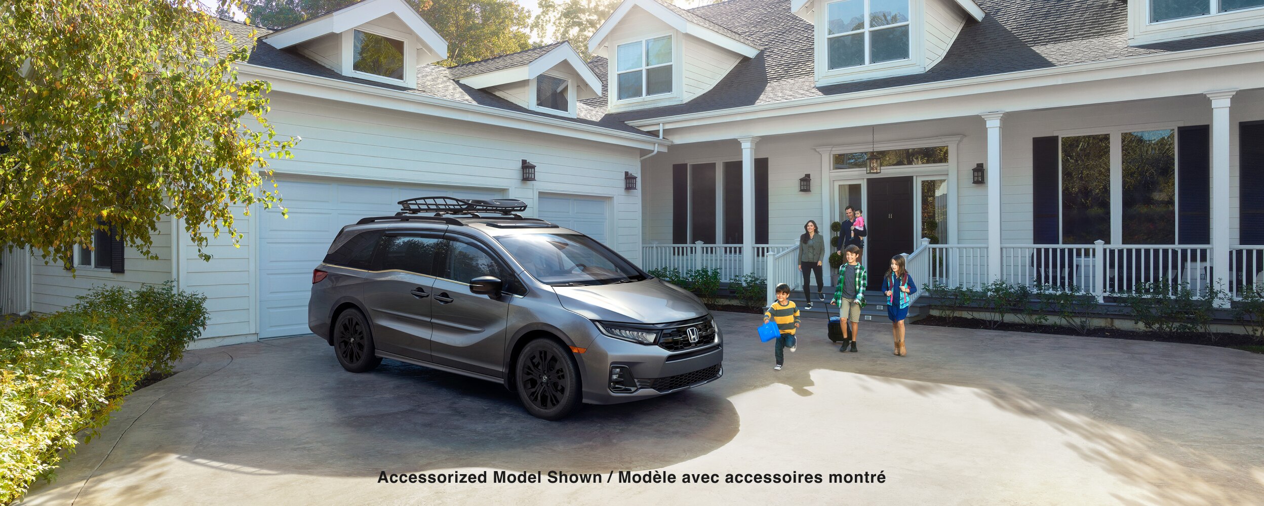 Vue latérale 3/4 avant d’une Odyssey grise stationnée dans une entrée. Une famille se dirige vers le véhicule.