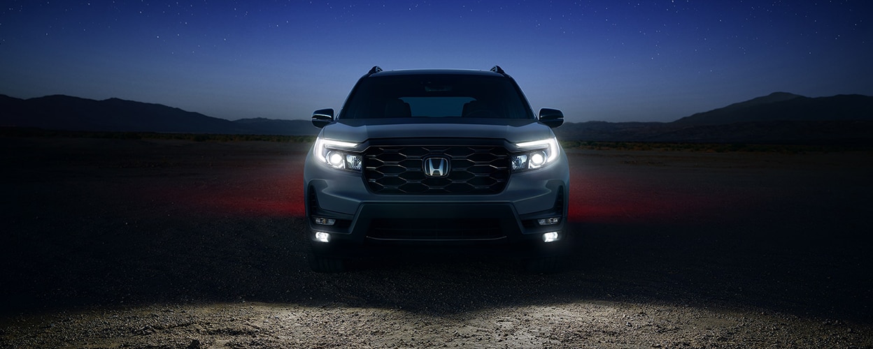 Head-on view of Honda Passport in desert at night with headlights on.