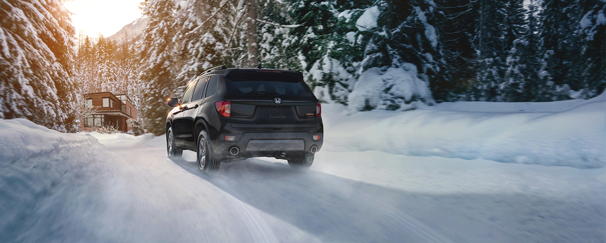 3/4 rear view of black Honda Passport driving on snowy forest road.