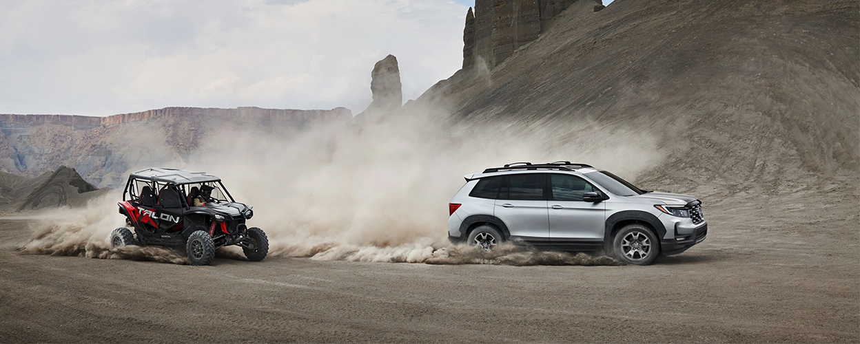 Side view of grey Honda Passport off-roading in desert. ATV follows closely behind.