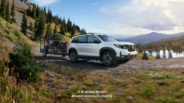 3/4 front side view of white Honda Passport towing an ATV in the forest.