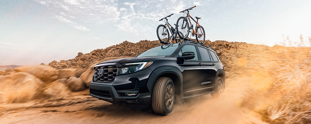 3/4 side front view of black Honda Passport desert off-roading with two bikes on the roof rails.