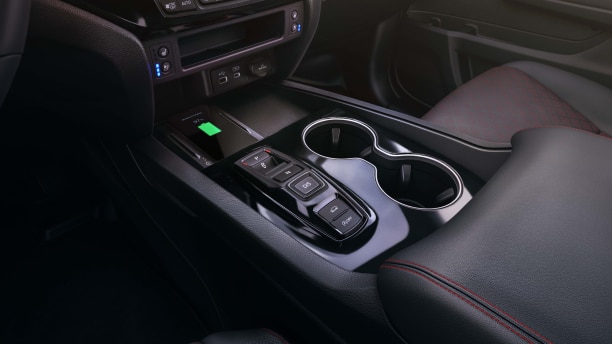 Medium closeup of centre console with arm rest, cup holders, buttons, and wireless charging pad.