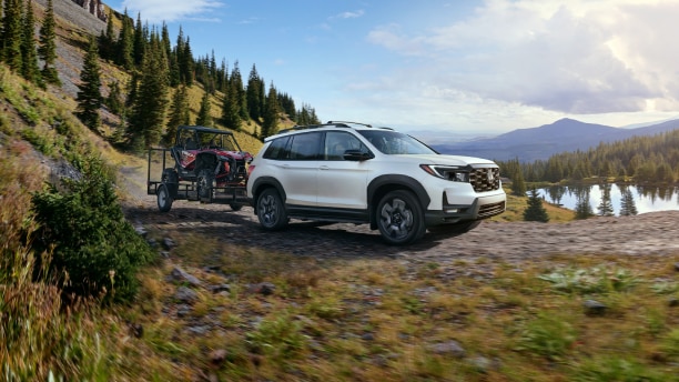 3/4 front side view of white Passport towing an ATV in the forest.