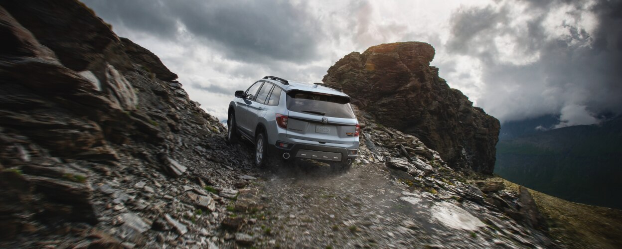 3/4 rear view of grey Passport driving up dirt road.