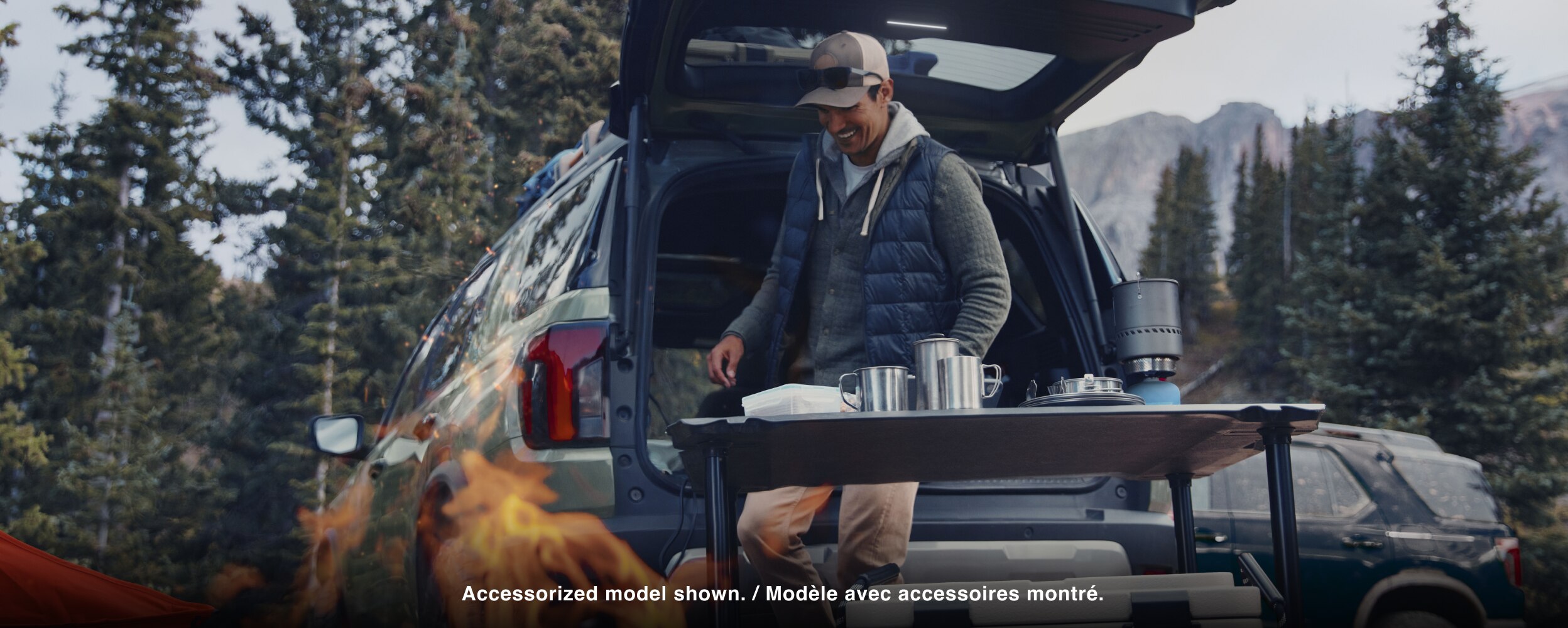 A man sets up a camping cookout behind a Passport. 