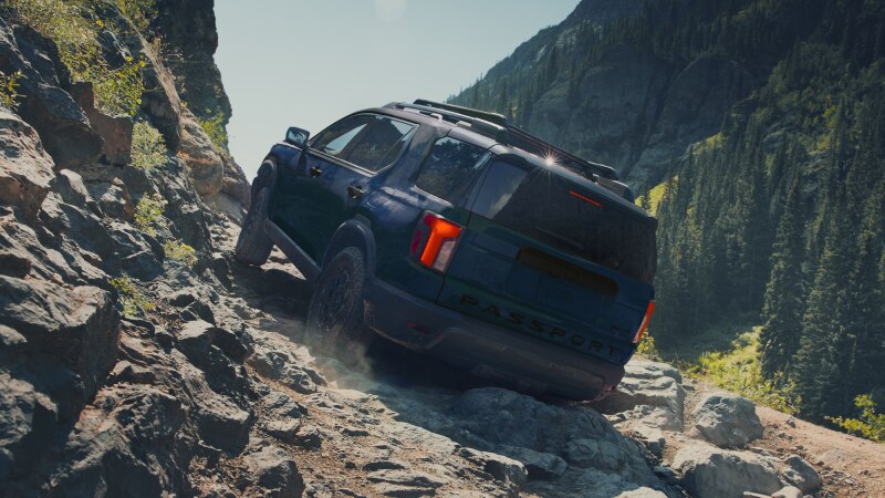 A blue Passport drives over rough mountain terrain. 