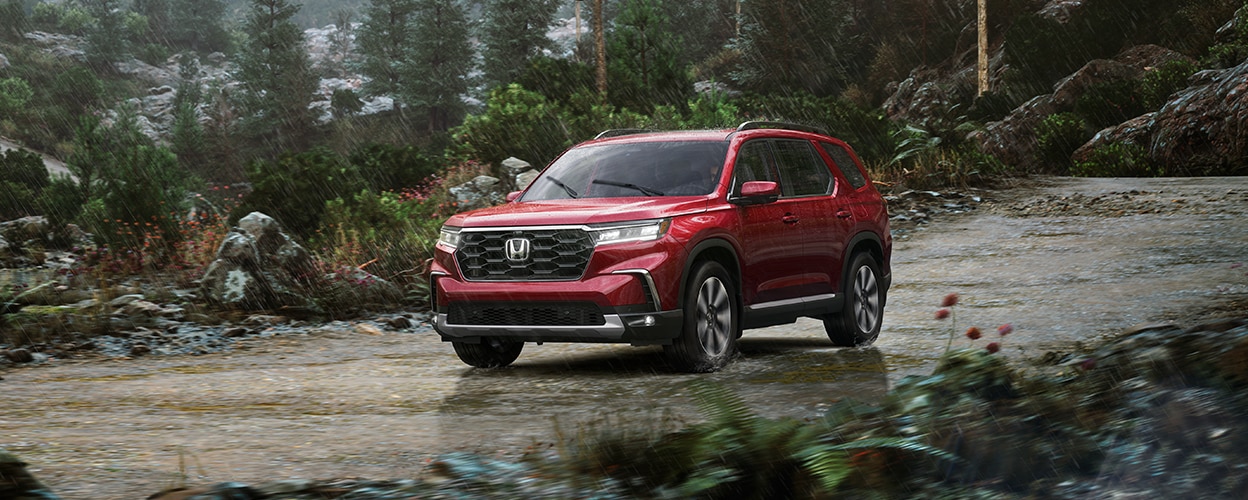 3/4 front view of red Pilot driving in the rain on a temperate rainforest road.