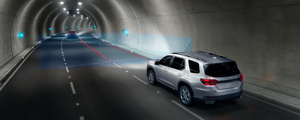 3/4 rear view of grey Pilot in driving in tunnel. Blue sensor lines and waves detect the lane divider lines. 