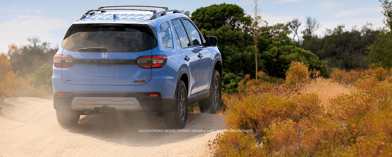 3/4 rear view of light blue Pilot driving on a desert dirt road amid desert plants.