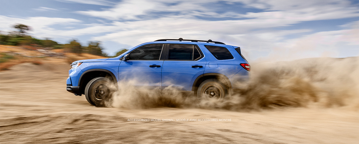 Medium wide sideview of light blue Pilot driving on a desert plain kicking up dust.