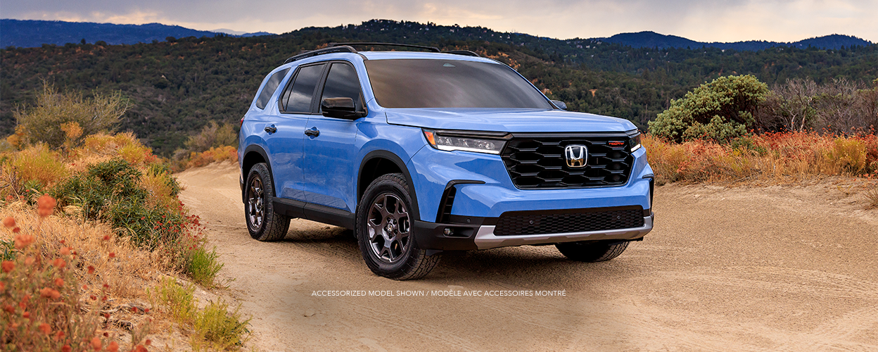 3/4 front view of light blue Pilot parked in middle of the desert amid desert plants.