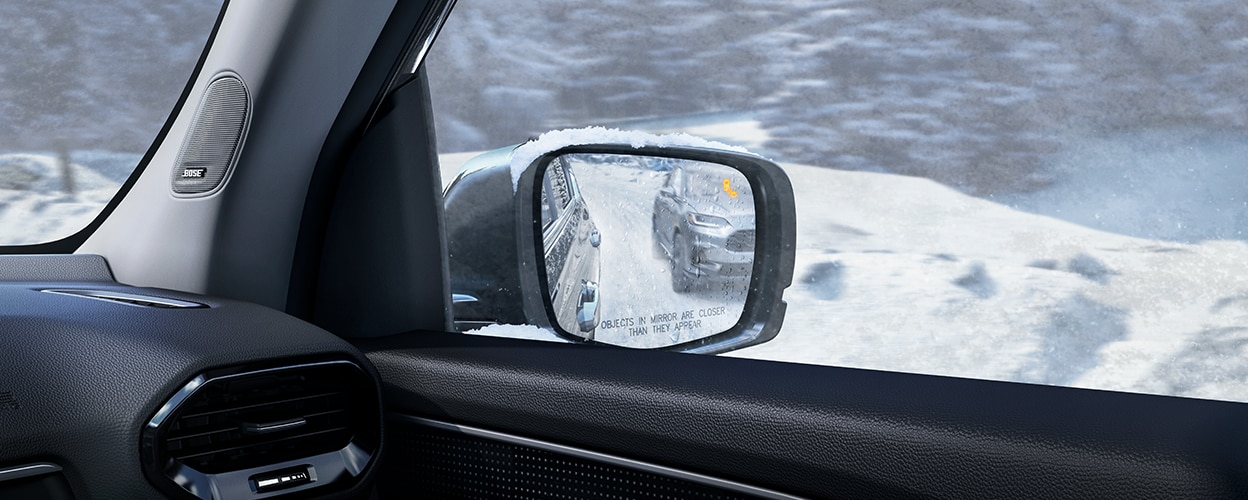 Honda Pilot View of door mirror, seen from inside, showing a vehicle in the reflection and an illuminated alert light.