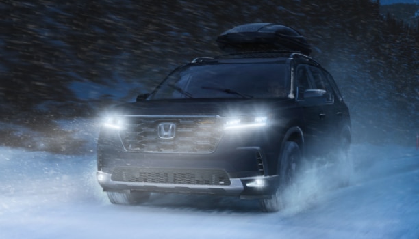 Plan de trois quarts avant d’un Pilot noir traversant la neige à toute vitesse sur une route forestière enneigée.