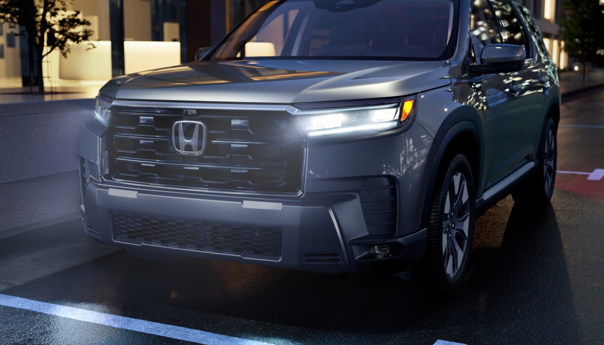 Vue avant d’un Pilot gris roulant de nuit en ville, phares allumés.